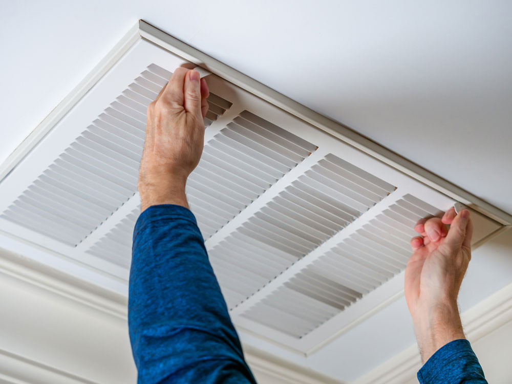 Man opening ceiling air vent to replace dirty hvac air